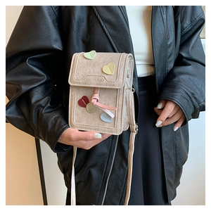 Detailed view of beige crossbody phone bag featuring colorful heart patches and stylish tassel