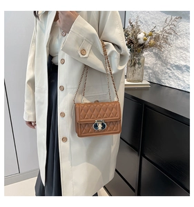 Gros plan du sac bandoulière marron matelassé avec chaîne dorée porté sur un trench-coat
