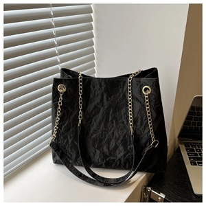 Detail of black pleated tote bag with embossed lettering and golden chain strap