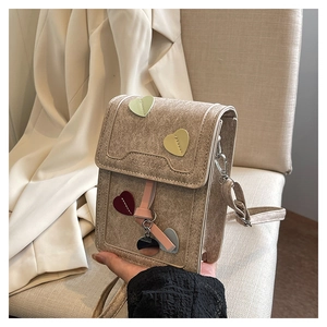 Detail of tan suede mini crossbody bag featuring heart patches and fashion bags engraving