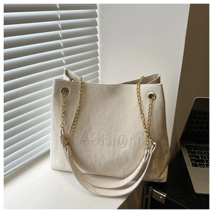 Detail of cream tote bag with FASHION embossing, gold chain, and wide shoulder strap