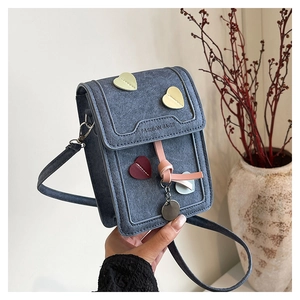 Detail of blue textured crossbody bag with colorful heart patches and gold charm