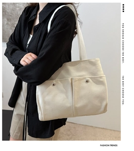Detail of cream canvas tote bag with front pockets and silver studs worn by model