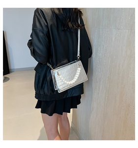 Detail of silver crocodile-patterned crossbody bag featuring chunky pearl chain accents