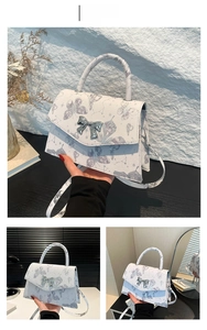 Detail of silver textured leather handbag with butterfly print and metallic bow buckle