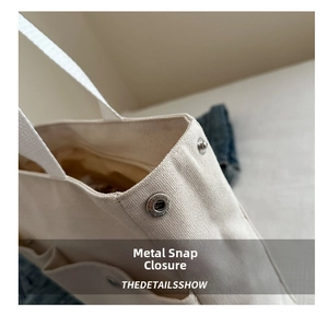 Detailed macro view of the metal snap button on a beige canvas tote bag side