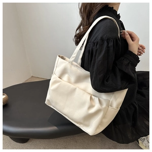 Vue latérale du grand sac cabas crème porté à l'épaule par un mannequin en noir