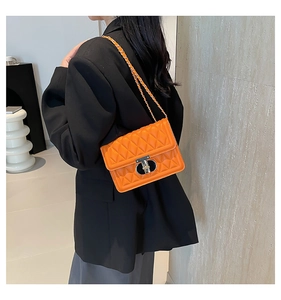 Sac bandoulière matelassé orange vif avec chaîne argentée porté par un mannequin en studio