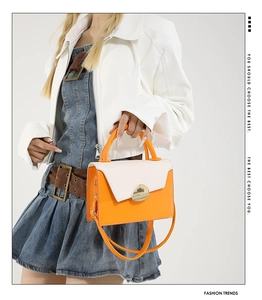 Detail of cream and orange contrast leather handbag with metallic buckle on white jacket