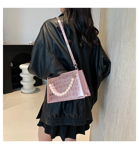 Detail view of a pink crocodile-patterned bag with decorative pearl handle chain