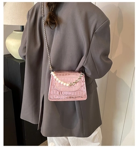 Détail du sac bandoulière rose à motif crocodile avec poignée en perles et chaîne