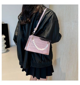 Detail of pink croc-pattern crossbody bag with large pearl handle shown on model