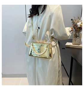 Detail of golden crocodile embossed square bag with pearl handle and metal strap