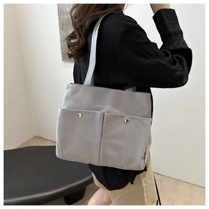 Detail of grey canvas tote bag featuring two front pockets and wide shoulder straps