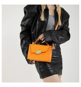 Close-up of bright orange leather handbag with gold pebble buckle on black leather outfit
