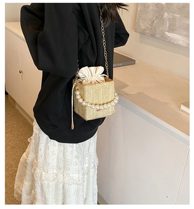 Detail of woven straw handbag featuring elegant pearl handle and secure drawstring liner