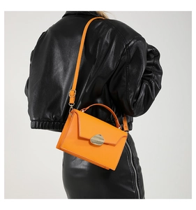 Detail of vibrant orange shoulder bag with unique gold metal buckle on leather