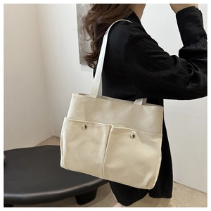 Detailed side view of beige canvas tote bag with front pockets and metal snaps for work