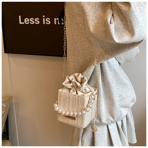 Detailed view of woven straw bag with pearl handle, gold chain, and drawstring closure