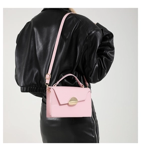Pink crossbody bag with leaf-shaped gold clasp worn by a model in a black leather outfit