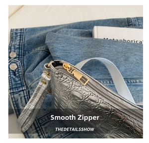 Detail of silver crocodile-embossed leather clutch with gold zipper and silver wrist strap