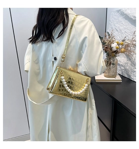 Detail of glossy gold faux croc texture and elegant large pearl chain strap on handbag