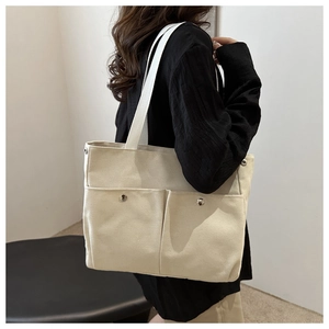 Détail du sac cabas en toile montrant des poches avant avec clous et bandoulière large