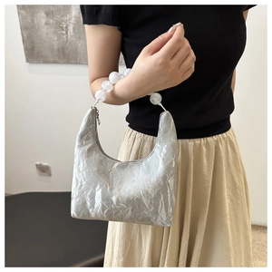 Close-up of silver hobo bag with metallic pleats and decorative white beaded handle
