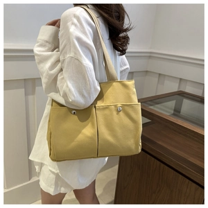 Close-up of a bright yellow canvas tote bag featuring double front pockets and metal snaps