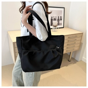 Détail d'un grand sac fourre-tout en nylon noir avec poche zippée plissée et large bandoulière