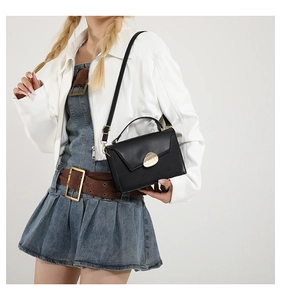Detail of elegant black patent leather bag featuring a gold teardrop metal buckle closure