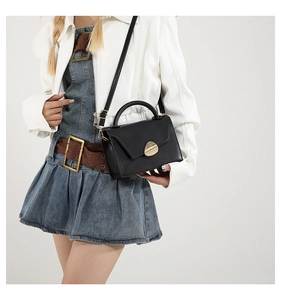 Detail of a black matte leather crossbody bag with a stylish gold shield metal buckle