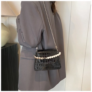 Mini black crocodile-textured crossbody bag with pearl and heart chain detail on a model