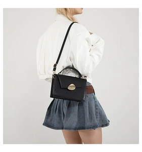 Model wearing a black leather handbag with a gold metal clasp and adjustable shoulder strap