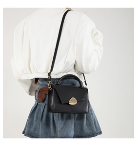 Rear view of a model wearing the black crossbody bag with its elegant gold oval clasp