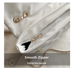 Detail of white quilted handbag showing gold zipper closure and metal chain strap