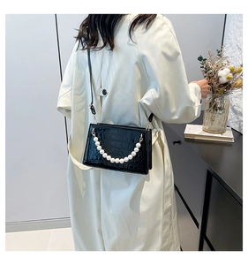 Detail of black faux crocodile leather bag with pearl chain handle on white coat