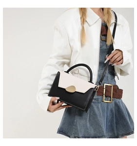 Détail du sac à bandoulière bicolore noir et blanc avec boucle dorée porté par un mannequin