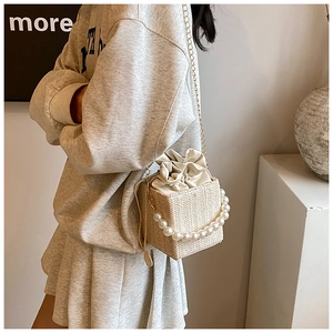 Close-up of woven bucket bag with large pearl handle and gold chain strap