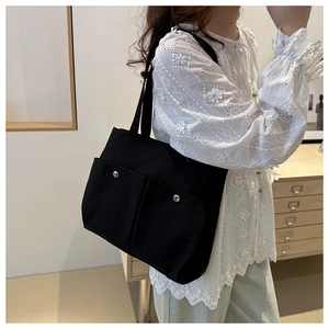Détail d'un sac cabas en toile noire avec de grandes poches avant et des boutons en métal
