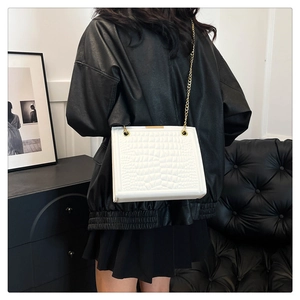 Close-up of a white crocodile pattern bag with a gold chain on a black leather coat