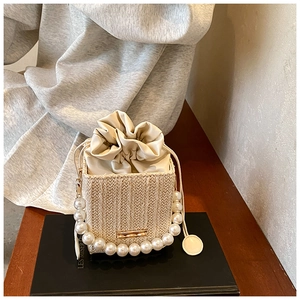 Detail of woven bucket bag with elegant pearl top handle and drawstring closure