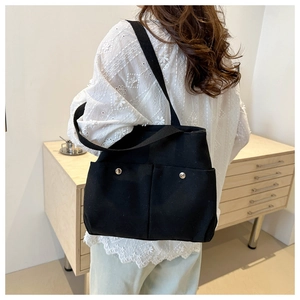 Détail du grand sac cabas en toile noire avec poches avant porté par un mannequin