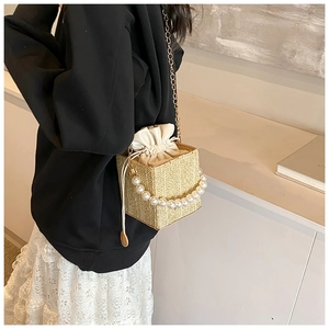 Detail of woven straw bucket bag featuring elegant pearl handle and gold chain strap