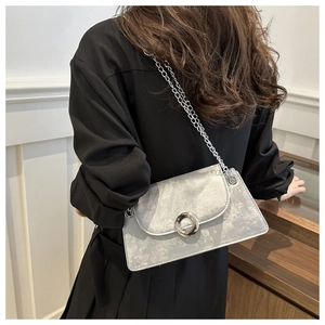 Sac à bandoulière texturé gris argenté avec chaîne porté par un mannequin sur mur blanc