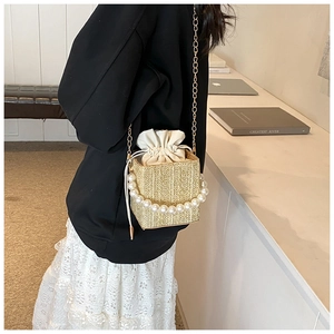 Detail of hand-woven straw bucket bag with large pearl handle and gold chain strap