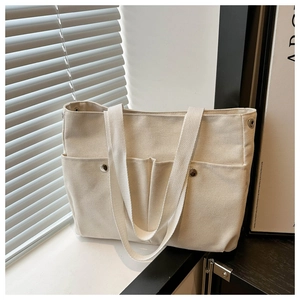 Vue détaillée du sac cabas en toile crème montrant le design multipoches et les rivets