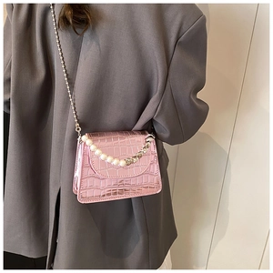 Pink mini crossbody bag with crocodile texture and pearl handle worn by model