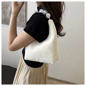 Detail of white pleated cloud bag featuring an marble-patterned beaded handle strap
