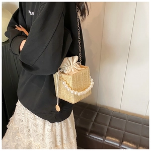 Straw bucket bag featuring pearl handle and gold chain strap shown on a model